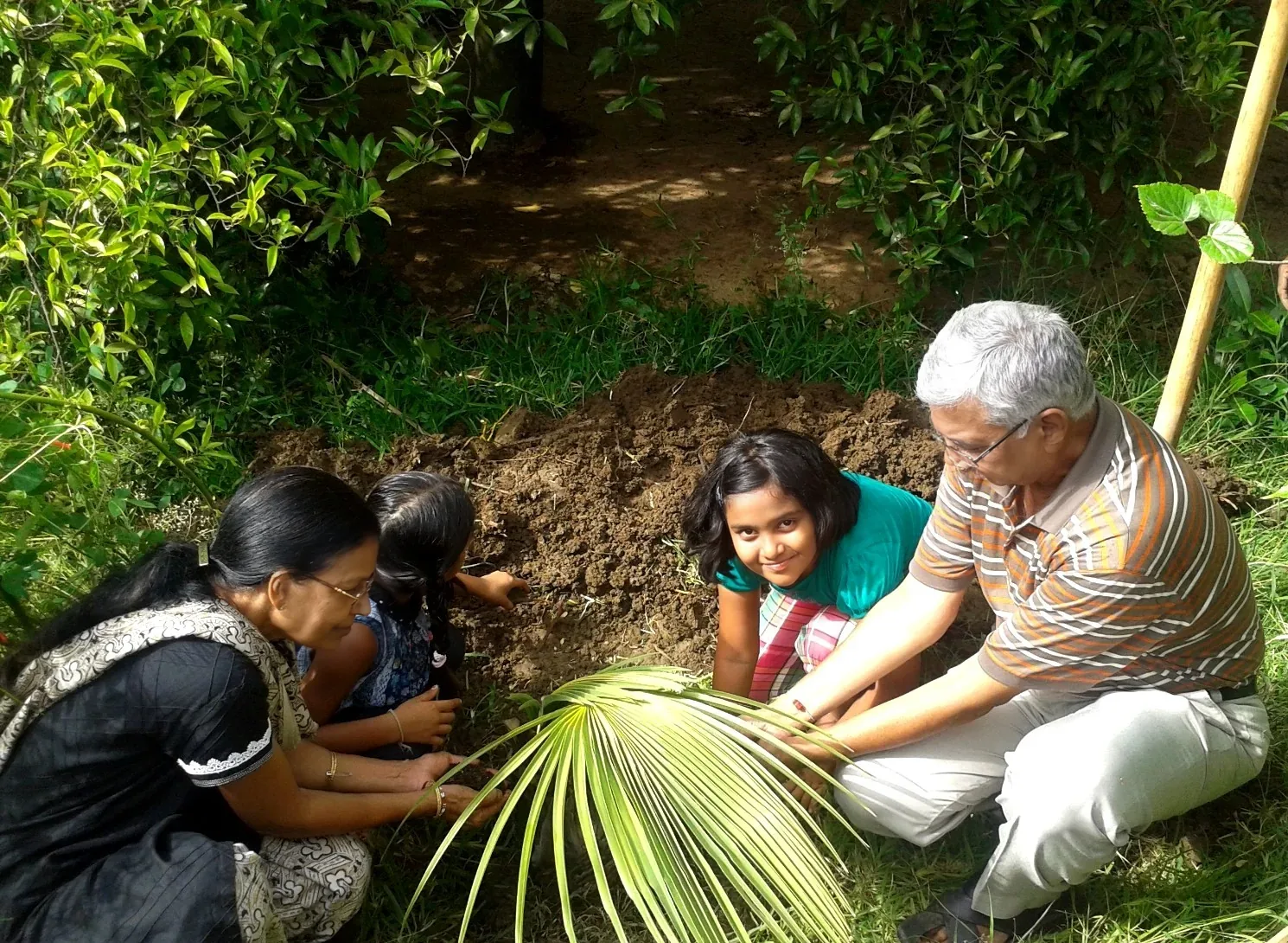 Grandparents and their granddaughters planting a palm sapling together at Save Farm